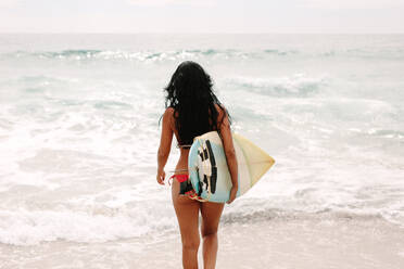 Rückansicht einer Frau im Bikini mit Surfbrett, die ins Meer geht und an einem Sommertag surfen geht. - JLPSF14970