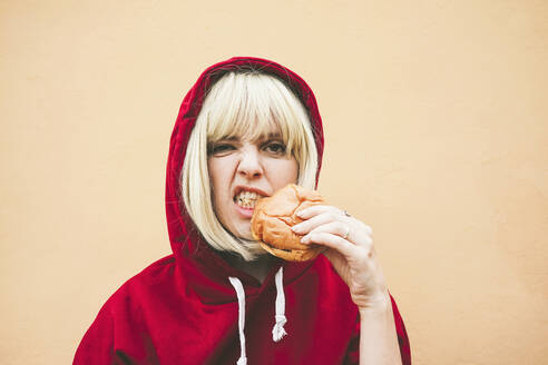 Frau mit rotem Kapuzenshirt isst Hamburger vor einer Pfirsichwand - SVCF00211