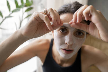 Woman peeling off face mask at home - ANAF00247