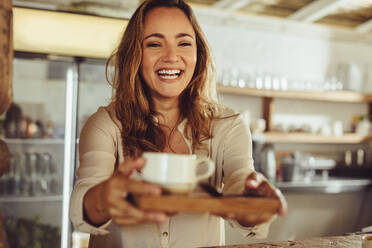 Lächelnde Frau, die hinter dem Tresen eines Cafés arbeitet. Glückliche junge Kellnerin, die den Kunden im Café Kaffee serviert. - JLPSF14979