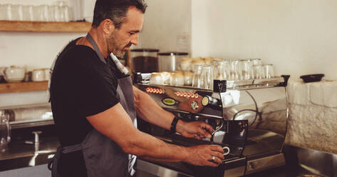 Barista, der eine Kaffeemaschine benutzt, um eine Tasse Kaffee zuzubereiten. Café-Mitarbeiter, der einen Kaffee zubereitet. - JLPSF14983