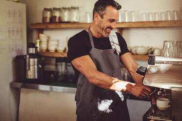 Lächelnder Kaffeehausangestellter, der mit einer Kaffeemaschine eine Tasse Kaffee zubereitet. Männlicher Barista, der in einem Café arbeitet. - JLPSF14985