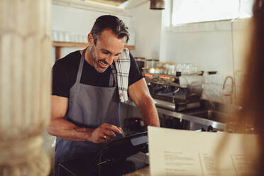 Café-Besitzer, der die Bestellung eines Kunden am Tresen entgegennimmt. Barista gibt die Kundenbestellung in den Kassencomputer ein. - JLPSF14990