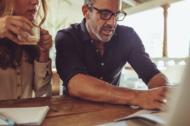 Man looking at laptop and discussing work with female colleague having coffee. Business people discussing new project over laptop at coffee shop. - JLPSF15003