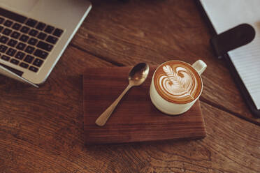 Draufsicht auf Tasse heißen Cappuccino Kunst Kaffee auf Holztisch mit einem Laptop und Molkerei auf der Seite. Tasse Milchkaffee mit Milchschaum Kunstmuster auf Cafe Tisch. - JLPSF15005