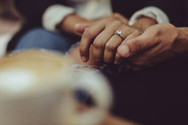 Close-up of couple holding hands at cafe together. Man holding hand woman wearing engagement ring. - JLPSF15011