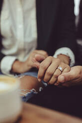 Loving couple holding hands at coffee shop together. Close-up of a man holding hand of his woman with an engagement ring. - JLPSF15012