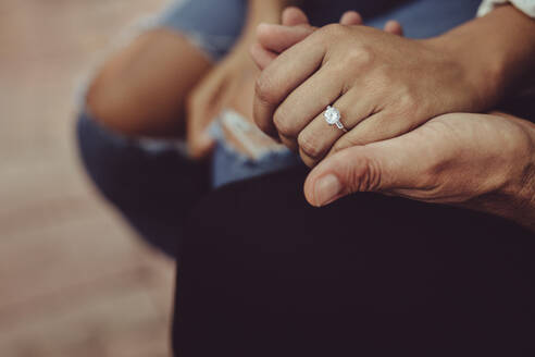 Nahaufnahme einer Frau mit Verlobungsring, die die Hand ihres Mannes hält. Verheiratetes Paar sitzt zusammen und hält sich die Hände. - JLPSF15013