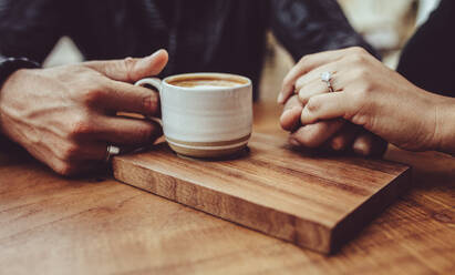 Close-up of loving couple holding hands at coffee shop. Man holding hand of his wife while having coffee at a cafe - JLPSF15014