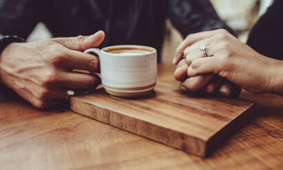 Nahaufnahme eines verliebten Paares, das sich in einem Café an den Händen hält. Ein Mann hält die Hand seiner Frau, während er in einem Café Kaffee trinkt - JLPSF15014