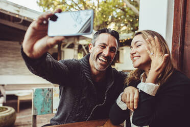 Ein Mann macht ein Selfie mit einer Frau, die ihren Verlobungsring zeigt, während sie in einem Café sitzt. Ein verliebtes Paar macht ein Selfie mit dem Verlobungsring. - JLPSF15017