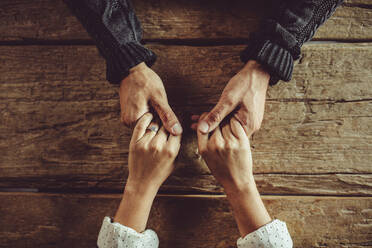 Directly above shot of couple sitting around table holding hands. Close-up shot of man and woman in love holding hands over a wooden table. - JLPSF15019