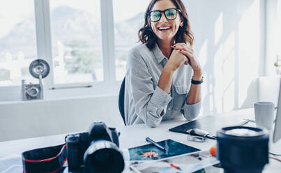 Eine weibliche Fotoredakteurin sitzt an ihrem Schreibtisch, eine Fotografin schaut in die Kamera und lächelt in ihrem Büro. - JLPSF15039
