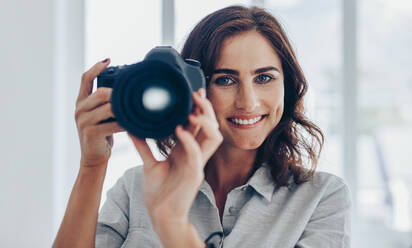 Beautiful young female photographer with dslr camera photographing. Happy woman shooting with professional camera. - JLPSF15045