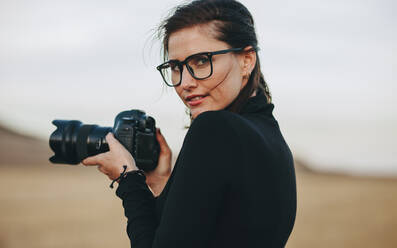 Junge Fotografin beim Fotografieren im Freien. Kaukasische Frau in Freizeitkleidung hält eine DSLR-Kamera. - JLPSF15063