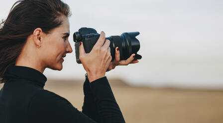 Side view of female photographer shooting with dslr camera outdoors. Woman having a outdoors photo shoot. - JLPSF15066