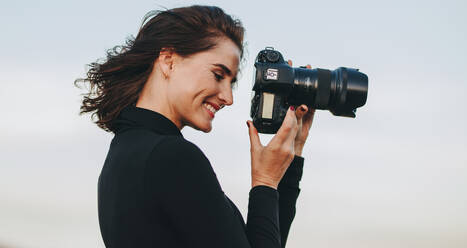 Professionelle Fotografin mit Spiegelreflexkamera beim Fotografieren. Junge Frau mit Kamera beim Fotografieren im Freien. - JLPSF15067