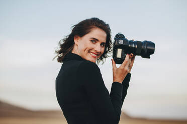Positive photographer enjoying photo shooting outdoors. Young woman in casual holding a photo camera and smiling. - JLPSF15068