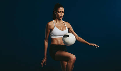 Fußballspielerin, die sich auf Jongliertechniken konzentriert. Frau in Sportkleidung jongliert einen Ball auf ihrem Knie vor dunklem Hintergrund. - JLPSF15095