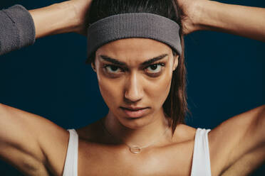 Close-up of a confident sportswoman with a headband staring at camera. Fit young woman in sportswear looking at camera. - JLPSF15106