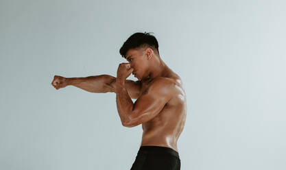 Seitenansicht eines muskulösen Sportlers, der im Studio Boxen trainiert. Männlicher Athlet, der Schattenboxen vor weißem Hintergrund übt. - JLPSF15126