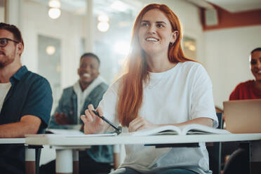 Pretty student paying attention in lecture. Girl listening to the teacher and smiling sitting in classroom. - JLPSF15137