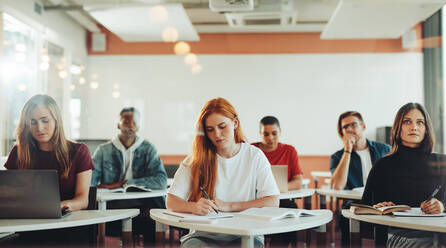 Männliche und weibliche Studenten sitzen im Klassenzimmer und machen sich während der Vorlesung Notizen. Studenten im Klassenzimmer einer High School. - JLPSF15138