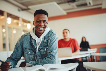 Afrikanischer Student sitzt im Klassenzimmer. Männlicher Student lächelt während der Vorlesung im Klassenzimmer der High School. - JLPSF15144