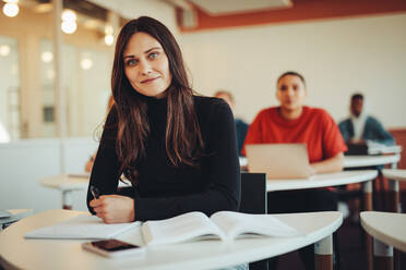 Portrait of a female student in classroom. High school sitting in a lecture looking at camera. - JLPSF15146