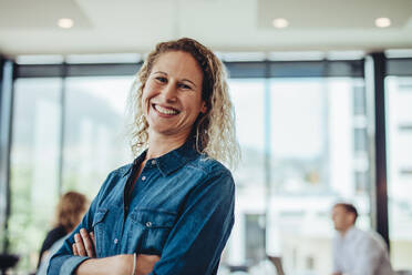 Positive business woman in meeting room with colleagues discussing in background. Confident female professional at board room meeting. - JLPSF15172