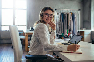 Smiling young woman taking note of orders from customers. Dropshipping business owner working in her office. - JLPSF15184