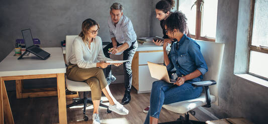 Diverse group of business people working together at a small office. Woman showing her digital tablet and discussing new business plan with coworkers. - JLPSF15197