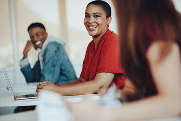 Lächelnde Schülerin im Gespräch mit Mitschülern im Klassenzimmer. Schüler unterhalten sich im Klassenzimmer einer High School. - JLPSF15200