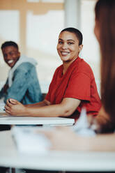 Lächelnde Studentin sitzt am Schreibtisch im Klassenzimmer der High School. Mädchen mit kurzen Haaren lächelt im Klassenzimmer der Universität. - JLPSF15201