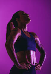 Nahaufnahme einer fitten Frau beim Fitnesstraining. Porträt einer Sportlerin auf lila Hintergrund mit Händen auf der Hüfte. - JLPSF15230