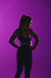 Porträt einer Sportlerin beim Training. Frau in Fitnesskleidung mit Händen auf der Hüfte auf lila Hintergrund. - JLPSF15232