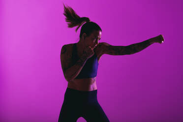 Focussed athlete doing punching exercises. Portrait of a muscular woman training in martial arts. - JLPSF15237