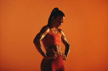 Monochromes Fitness-Porträt einer Bodybuilderin, die auf einem orangefarbenen Hintergrund trainiert. - JLPSF15253