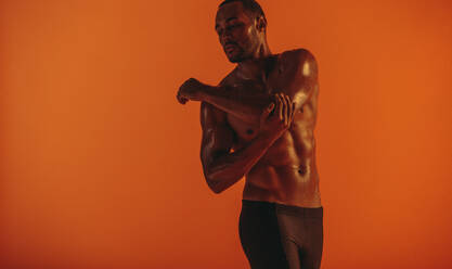 Abgeschnittene Aufnahme eines muskulösen Mannes mit nacktem Oberkörper auf orangefarbenem Hintergrund. Monochromes Porträt eines fitten Mannes beim Workout. - JLPSF15263