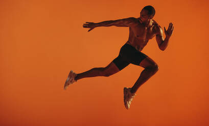 Muscular athlete looking back while running forward. African american athlete doing fitness workout on orange background. - JLPSF15265