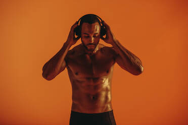 Nackter muskulöser Athlet, der während des Trainings eine Pause macht und Musik hört. Porträt eines fitten Mannes, der mit drahtlosen Kopfhörern Musik hört. - JLPSF15268