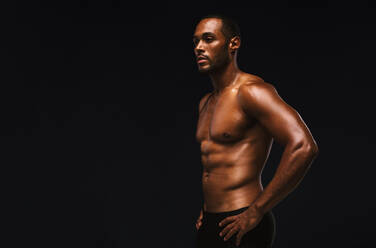 Porträt eines afroamerikanischen Mannes auf schwarzem Hintergrund. Muskulöser Athlet mit nacktem Oberkörper und Händen auf der Hüfte stehend. - JLPSF15322