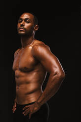 Close up portrait of muscular african american athlete. Side view of fit man standing on black background with hands on waist. - JLPSF15323