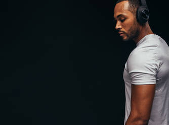 Muskulöser Mann, der mit drahtlosen Kopfhörern Musik hört. Beschnittene Aufnahme eines fitten Mannes auf schwarzem Hintergrund. - JLPSF15328