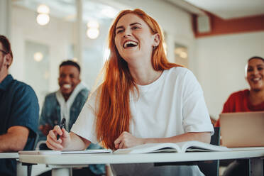 Eine Studentin lacht während einer Vorlesung in der Klasse. Ein Mädchen sitzt am Schreibtisch und lächelt während des Glases. - JLPSF15369