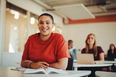 Porträt eines Mädchens, das in einem Klassenzimmer der Universität sitzt und lächelt. Eine Studentin im Hörsaal schaut in die Kamera und lächelt. - JLPSF15378