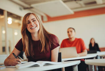 Porträt eines hübschen, lächelnden Mädchens in einem Universitätsklassenzimmer. Ein Student im Hörsaal einer High School schaut in die Kamera und lächelt. - JLPSF15379