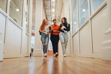 Eine Gruppe von Frauen geht in einem College-Korridor spazieren. Lächelnde Studentinnen auf dem Universitätscampus. - JLPSF15392