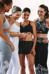 Close up of fitness women looking at a fitness app for an online workout. Cheerful young women in fitness wear relaxing after workout using a mobile phone. - JLPSF15433