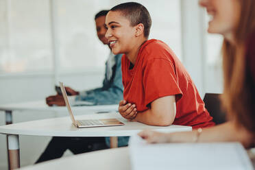 Lächelnde Studentin sitzt am Schreibtisch mit Laptop in der High School Klassenzimmer. Mädchen mit kurzen Haaren lächelnd während der Vorlesung in der Universität Klassenzimmer. - JLPSF15438